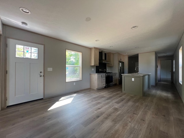 440 High St, Sanford, ME 04073 - kitchen featuring stainless steel gas stove, wall chimney exhaust hood, light wood-style floors, light countertops, and a kitchen island with sink