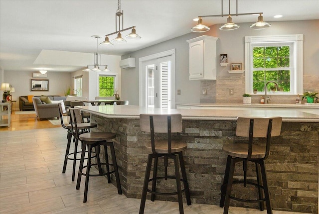 59 Sanderson Rd, Poland, ME 04274 - kitchen with an AC wall unit, white cabinetry, decorative backsplash, light countertops, and hanging light fixtures