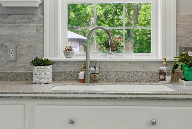 59 Sanderson Rd, Poland, ME 04274 - detailed view of decorative backsplash, white cabinetry, a sink, and light stone counters