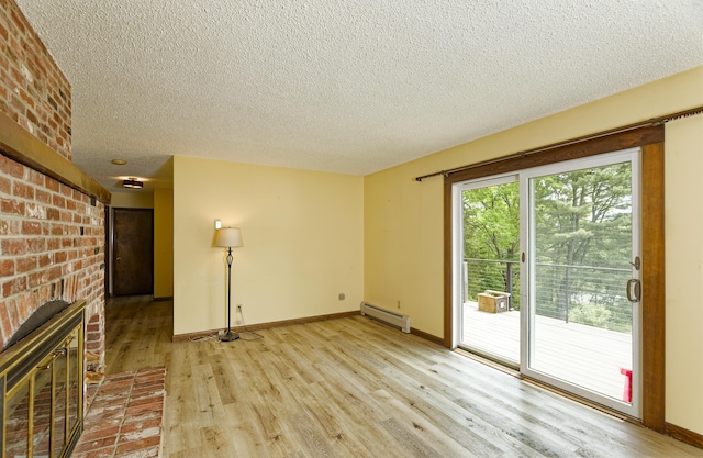 56 Borland Hill Rd, Nobleboro, ME 04555 - unfurnished living room with a baseboard heating unit, light wood-style floors, a textured ceiling, a fireplace, and brick wall