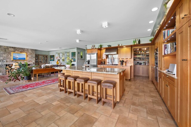 72 Vine St, South Berwick, ME 03908 - kitchen with stainless steel fridge with ice dispenser, stone finish floors, wall chimney range hood, a breakfast bar, and a center island with sink