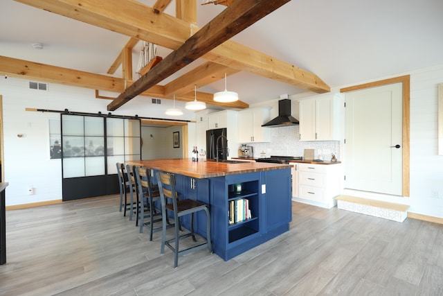 32 Water St, Lubec, ME 04652 - kitchen with butcher block countertops, wall chimney range hood, a barn door, freestanding refrigerator, and white cabinets