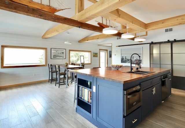 32 Water St, Lubec, ME 04652 - kitchen featuring butcher block counters, a barn door, light wood-type flooring, beamed ceiling, and a kitchen island with sink