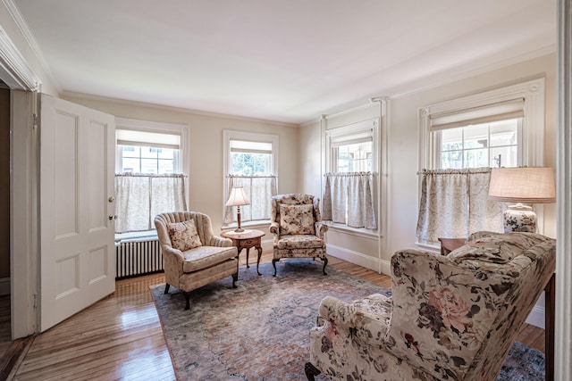sitting room with radiator, crown molding, wood finished floors, and baseboards