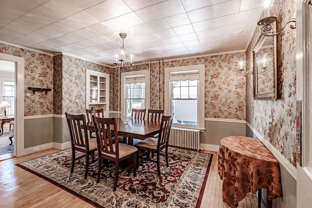 dining area with wood finished floors, crown molding, wallpapered walls, and radiator heating unit