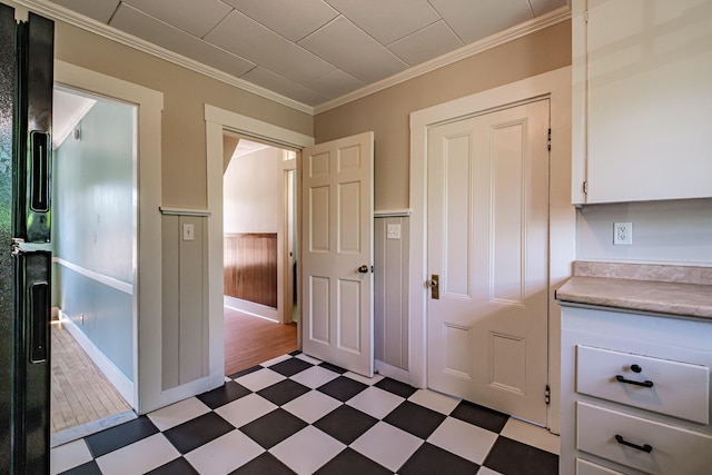 kitchen with light flooring, wainscoting, light countertops, white cabinetry, and ornamental molding