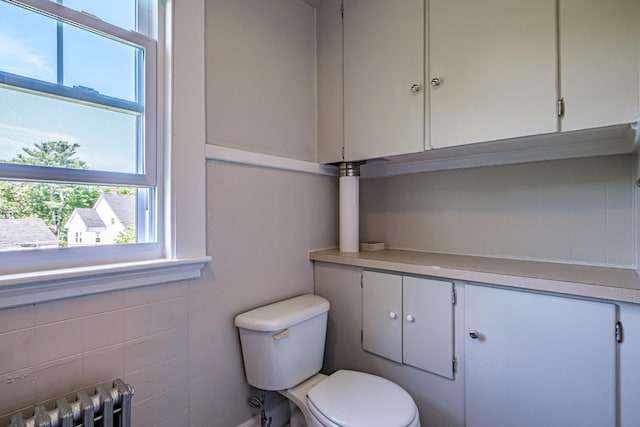half bathroom featuring radiator, toilet, vanity, and tile walls