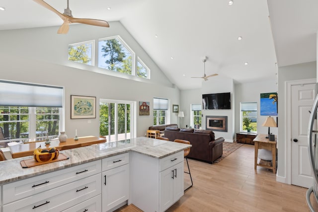 29 Bay Field Dr, Woolwich, ME 04579 - kitchen with ceiling fan, high vaulted ceiling, white cabinetry, a glass covered fireplace, and light stone counters
