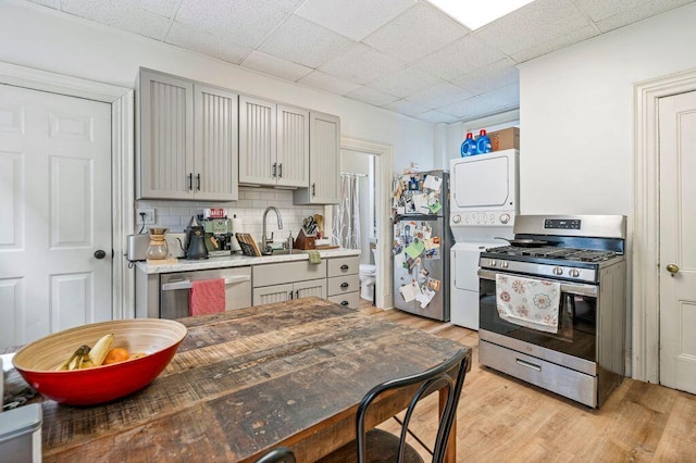 130 Emery St, Portland, ME 04102 - kitchen with stainless steel appliances, stacked washer / dryer, light wood-style flooring, decorative backsplash, and gray cabinets
