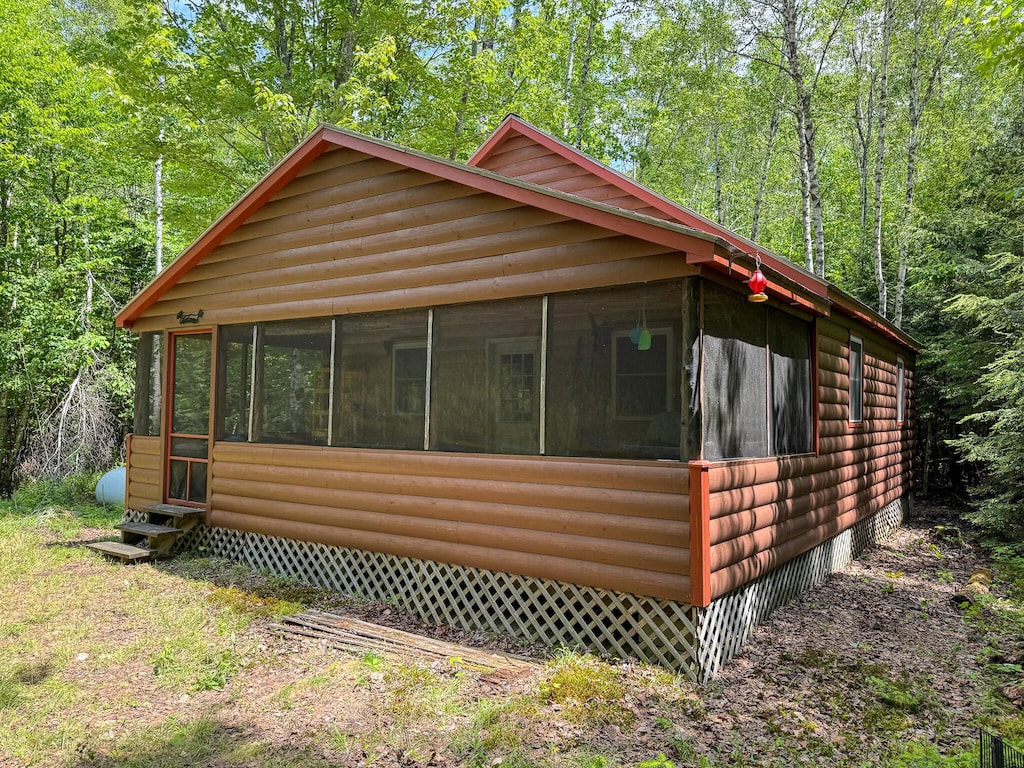 71 Wilderness Way, Burlington, ME 04417 - view of front facade with a sunroom, log veneer siding, a view of trees, and entry steps