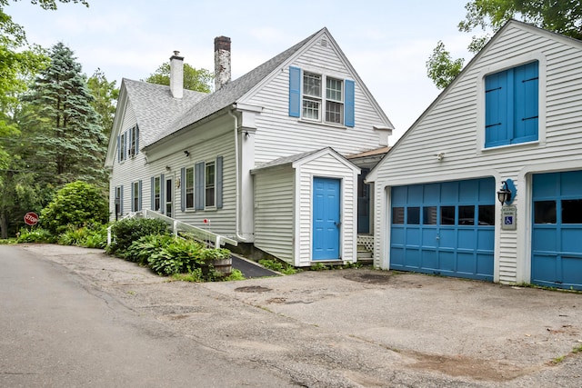 785 W Main St, Waldoboro, ME 04572 - view of front of house featuring a chimney, a garage, a shingled roof, and driveway