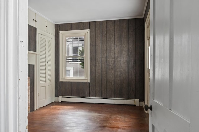 785 W Main St, Waldoboro, ME 04572 - unfurnished bedroom featuring a baseboard heating unit, wood finished floors, wood walls, crown molding, and a closet