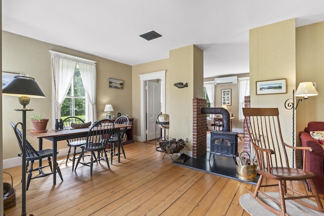 145 Pork Point Rd, Bowdoinham, ME 04008 - dining space featuring a wood stove, a wall unit AC, wood-type flooring, baseboards, and wallpapered walls