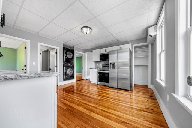 181 Webster St, Lewiston, ME 04240 - kitchen with appliances with stainless steel finishes, estacked washer and dryer, light wood-type flooring, white cabinets, and a drop ceiling