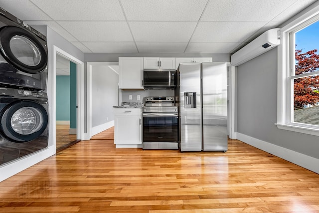181 Webster St, Lewiston, ME 04240 - kitchen with appliances with stainless steel finishes, stacked washer / dryer, a paneled ceiling, light wood-type flooring, and white cabinets