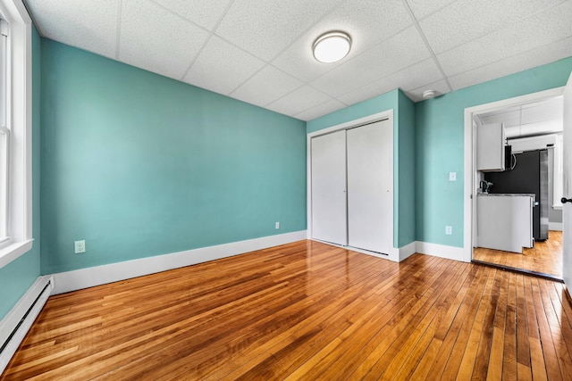 181 Webster St, Lewiston, ME 04240 - unfurnished bedroom featuring a baseboard radiator, a closet, a drop ceiling, baseboards, and hardwood / wood-style flooring
