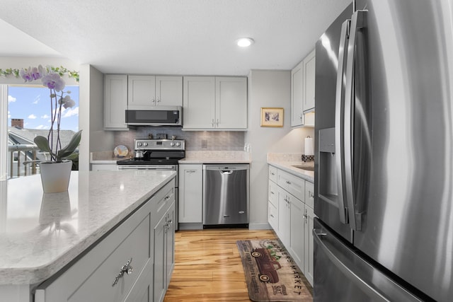 1 Seacliff Ave Unit 3D, Old Orchard Beach, ME 04064 - kitchen with stainless steel appliances, light wood-style flooring, decorative backsplash, gray cabinets, and light stone counters