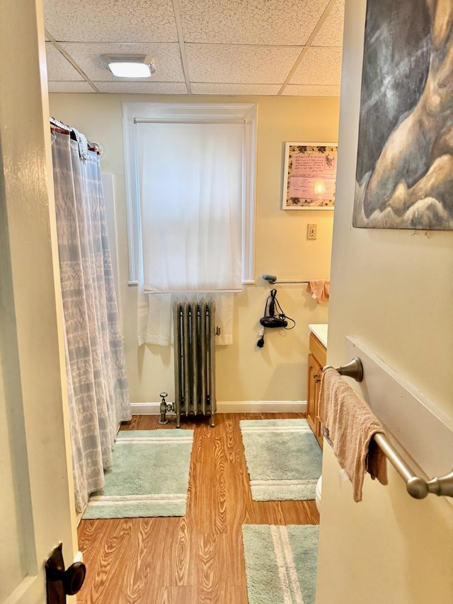 91 Washburn Ave, Portland, ME 04102 - bathroom with radiator heating unit, vanity, wood finished floors, a paneled ceiling, and a shower with curtain