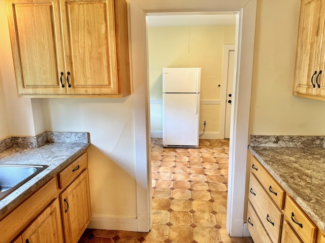 91 Washburn Ave, Portland, ME 04102 - kitchen featuring freestanding refrigerator, light flooring, stone counters, baseboards, and a sink