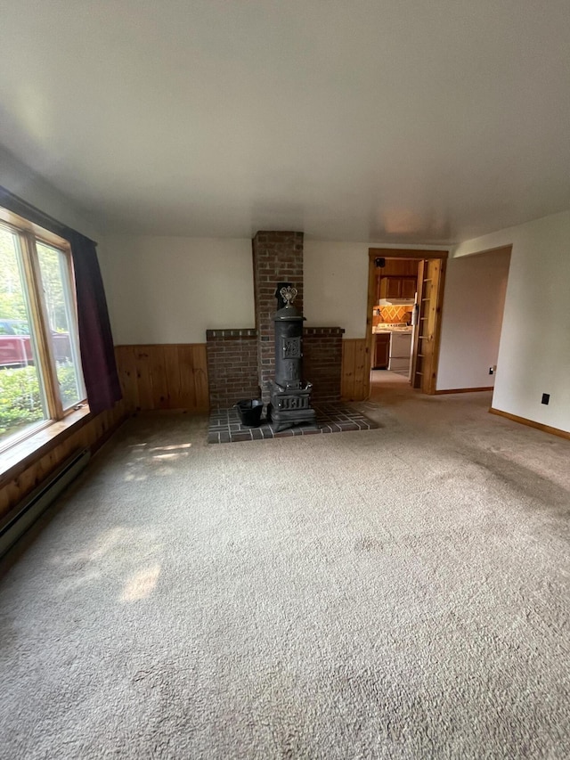 386 Lower Flying Point Rd, Freeport, ME 04032 - unfurnished living room featuring carpet flooring, a wainscoted wall, wood walls, a wood stove, and a baseboard heating unit