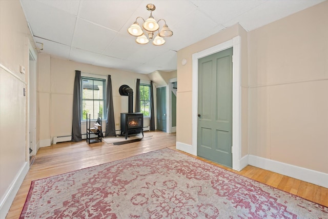 133 Front St, Old Town, ME 04468 - unfurnished living room with a wood stove, wood finished floors, a chandelier, and baseboard heating
