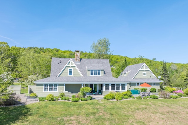 321 Beech Hill Rd, Northport, ME 04849 - back of property with a chimney, a lawn, a wooded view, a patio, and roof with shingles