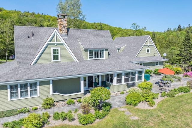 321 Beech Hill Rd, Northport, ME 04849 - back of house with roof with shingles, a chimney, a patio area, a sunroom, and a lawn