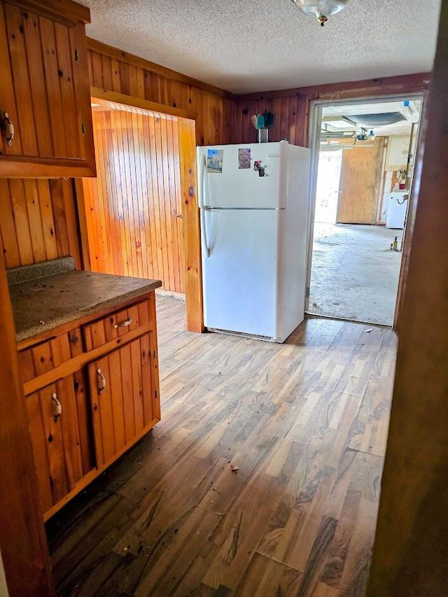 230 Todds Corner Rd, Saint Albans, ME 04971 - kitchen featuring freestanding refrigerator, a textured ceiling, wood walls, light wood-style floors, and brown cabinets