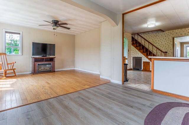 982 Main St, Grand Isle, ME 04746 - unfurnished living room featuring stairs, wood finished floors, ceiling fan, a glass covered fireplace, and baseboards