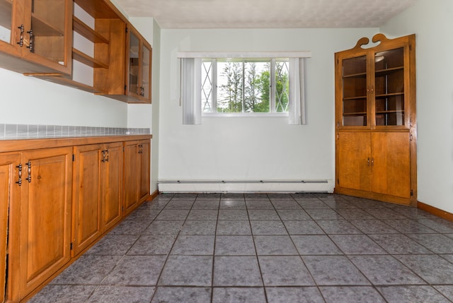 982 Main St, Grand Isle, ME 04746 - kitchen featuring a baseboard radiator, light countertops, brown cabinetry, glass insert cabinets, and baseboards