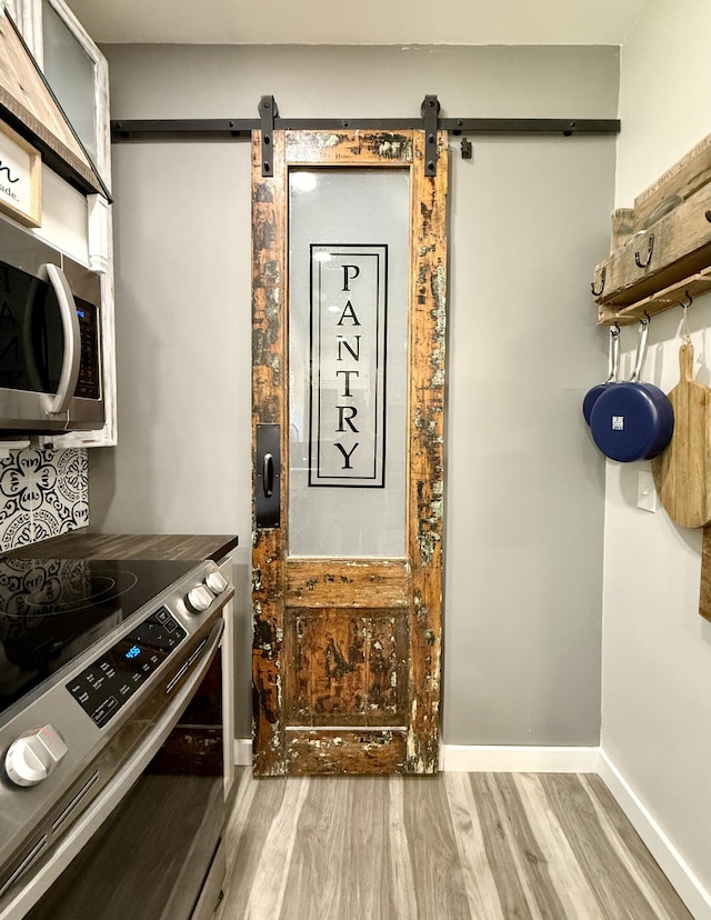 88 Union St, Calais, ME 04619 - kitchen with appliances with stainless steel finishes, a barn door, wood finished floors, and baseboards