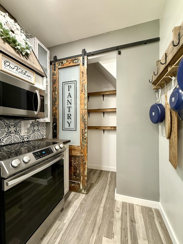 88 Union St, Calais, ME 04619 - kitchen with appliances with stainless steel finishes, light wood-style floors, a barn door, and baseboards