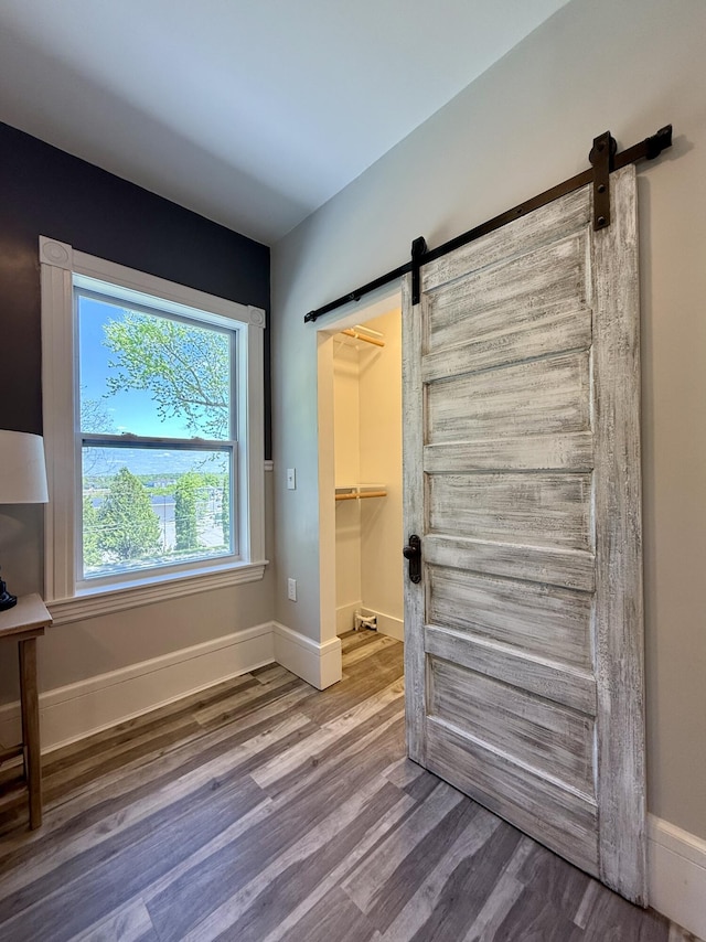 88 Union St, Calais, ME 04619 - unfurnished bedroom with a barn door, wood finished floors, a spacious closet, and baseboards