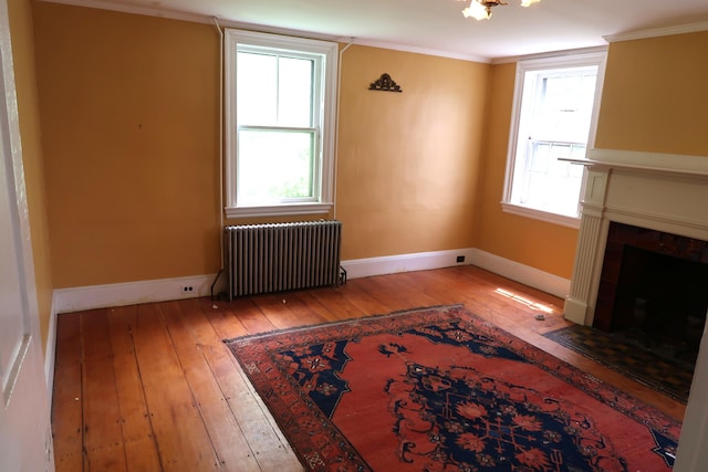7 Elm St, Augusta, ME 04330 - unfurnished living room featuring radiator heating unit, wood-type flooring, a fireplace with flush hearth, crown molding, and baseboards