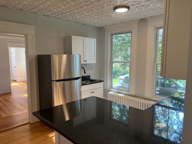 34 Birch St, Biddeford, ME 04005 - kitchen with radiator heating unit, freestanding refrigerator, an ornate ceiling, light wood-style flooring, and white cabinets