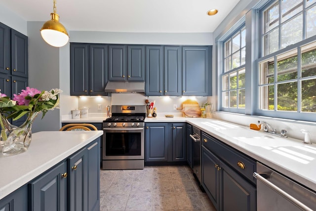33 Rocky Ln, Ogunquit, ME 03907 - kitchen with appliances with stainless steel finishes, under cabinet range hood, light countertops, blue cabinetry, and decorative light fixtures