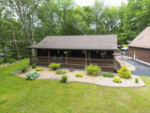 509 Upper Guinea Rd, Lebanon, ME 04027 - view of front facade with covered porch, a front lawn, roof with shingles, log exterior, and view of wooded area