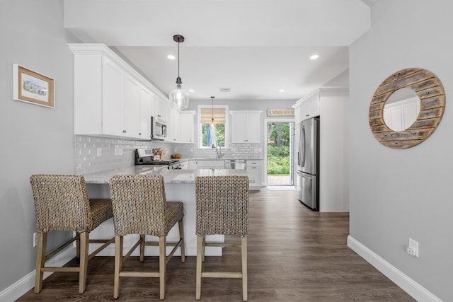46 Patriot Way Unit 135, Arundel, ME 04046 - kitchen featuring appliances with stainless steel finishes, a peninsula, tasteful backsplash, dark wood-type flooring, and light stone counters