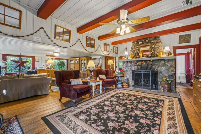 9 Dry Point Dr, Rome, ME 04963 - living area featuring hardwood / wood-style floors, beam ceiling, a stone fireplace, ceiling fan, and wooden walls