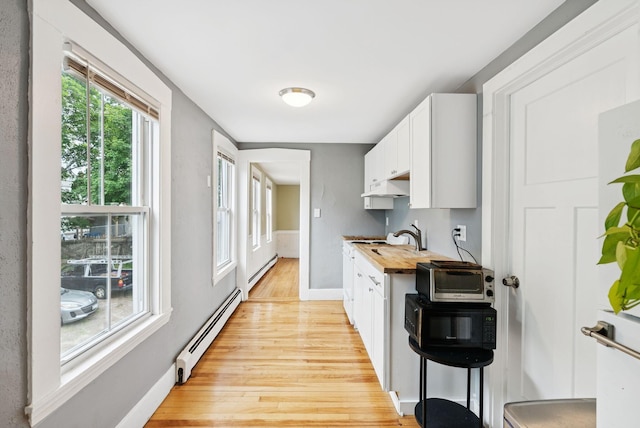 82 Winter St, Portland, ME 04102 - kitchen with a baseboard heating unit, butcher block countertops, light wood finished floors, baseboards, and white cabinets