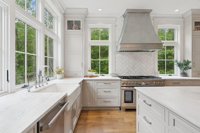 38 Fieldstone Ln, Falmouth, ME 04105 - kitchen with custom range hood, stainless steel appliances, tasteful backsplash, glass insert cabinets, and light wood-style flooring