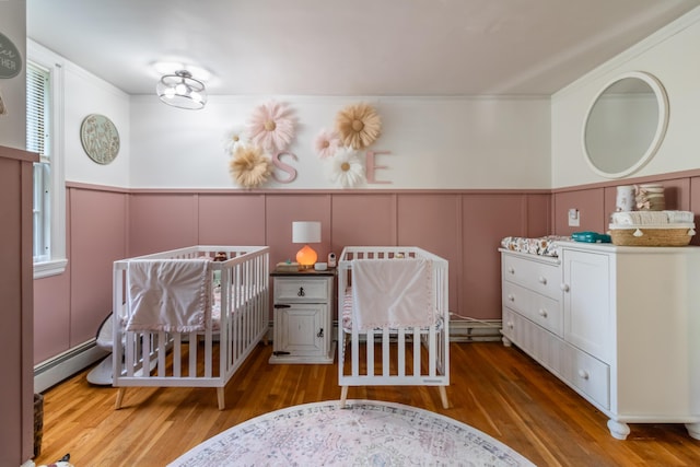 166 Franklin St, Bucksport, ME 04416 - bedroom featuring a decorative wall, a baseboard radiator, wood finished floors, a wainscoted wall, and a nursery area