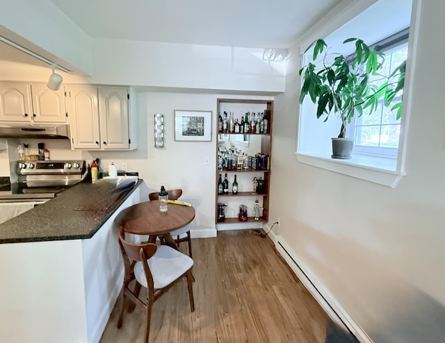 245 Broadway Unit 106, South Portland, ME 04106 - kitchen with under cabinet range hood, wood finished floors, white cabinetry, a breakfast bar, and stove