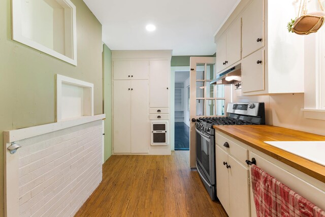 419 River Rd, Newcastle, ME 04553 - kitchen with stainless steel range with gas stovetop, under cabinet range hood, wood finished floors, wood counters, and white cabinetry