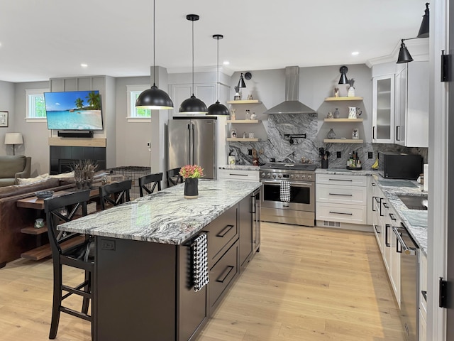 132 Mineral Spring Rd Unit 1, Windham, ME 04062 - kitchen featuring stainless steel appliances, wall chimney range hood, open shelves, decorative backsplash, and a breakfast bar area