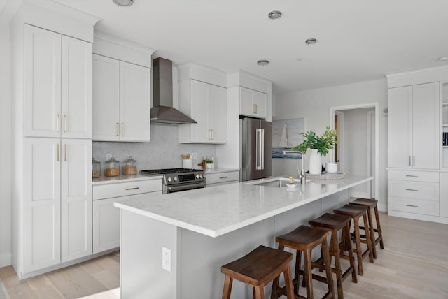 387 Commercial St Unit 527, Portland, ME 04101 - kitchen featuring wall chimney range hood, appliances with stainless steel finishes, white cabinetry, a breakfast bar area, and a kitchen island with sink