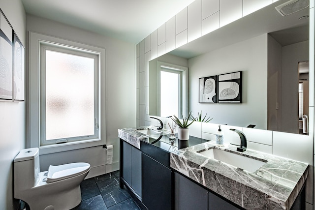 156 Oxford St, Portland, ME 04101 - bathroom featuring toilet, double vanity, marble look tiles, and baseboards