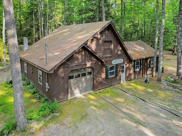 21 Heritage Ln, Orland, ME 04472 - rustic home featuring a shingled roof, an attached garage, dirt driveway, and a view of trees