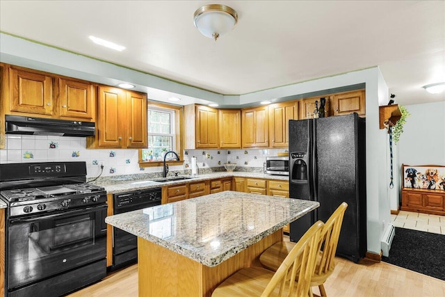 21 Heritage Ln, Orland, ME 04472 - kitchen with black appliances, under cabinet range hood, light stone counters, a kitchen breakfast bar, and tasteful backsplash