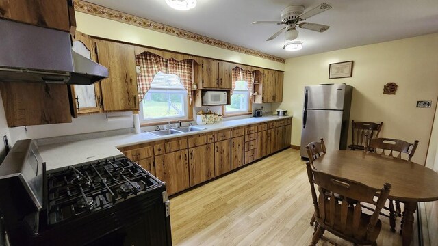 177 Ohio St, Millinocket, ME 04462 - kitchen with freestanding refrigerator, black gas stove, exhaust hood, brown cabinets, and light wood-style flooring